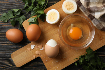 Board with boiled eggs, napkin and parsley on wooden background