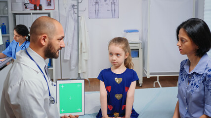Doctor talking with child's mother and holding a green screen tablet.Healthcare specialist with chroma key notebook isolated mockup replacement screen. Easy keying medicine medical related theme.