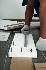 Furniture assembly process. Worker in overalls and white footwear. Using a screwdriver. Do it yourself.