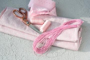 Striped cotton fabric, scissors, threads, elastic band and pink lace on a light gray background.  Fashioner market concept