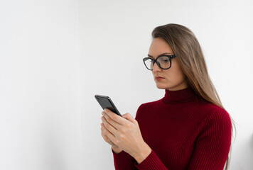 Fototapeta premium Young woman in glasses holding a phone on a white background. SMS and internet communication concept. Copy space