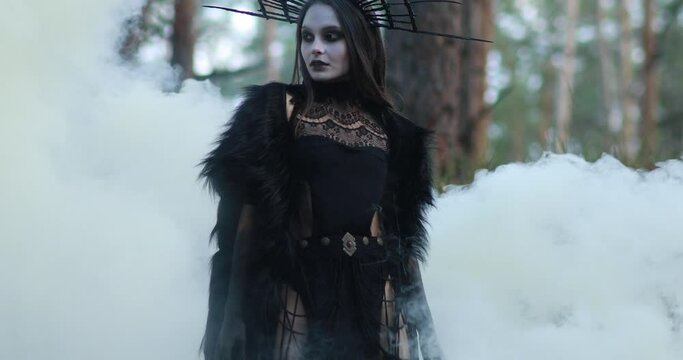 Woman in image of witch walks through smoke in forest.