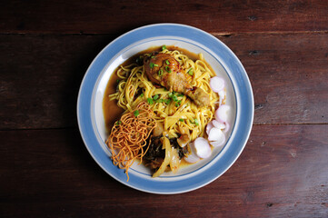 Traditional Northern Thai food (Khao Soi), spicy curry noodles soup with coconut milk and chicken in a bowl on wooden background, Asian food, Top view