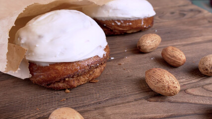 Two cinnamon bun with yoghurt cream in a paper craft package lying on a wooden background next to nuts