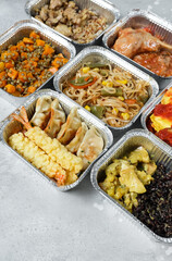 Takeout coronavirus food. Different aluminium lunch box with ravioli, curry chicken  rice, gyoza tempura, noodles vegetables, lentils with pumpkin. covid-19 takeaway  food delivery.