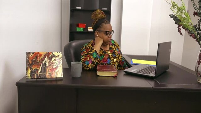 Black lady sitting at desk checking emails with discontentment