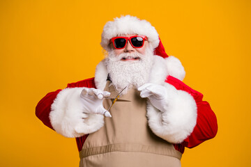 Close-up portrait of nice attractive cheerful cheery grey-haired Santa wearing apron cutting fixing beard beauty salon isolated bright vivid shine vibrant yellow color background