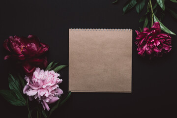 Beautiful peonies in dark colors and notebook. Black Floral background. Soft focus, copy space