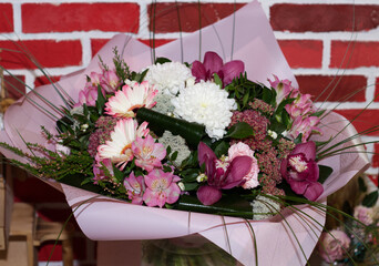 beautiful bouquet of bright pink, white flowers, orchids, chrysanthemums, prepackaged, in a flower shop, against a background of a brick wall. A bouquet for a holiday, celebration. Flower trade, 