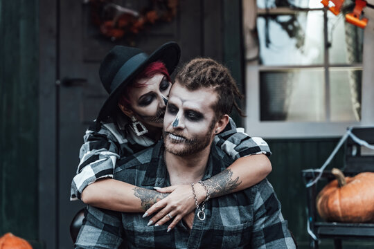 Scary love couple,man,woman.Family,mother,father celebrating halloween.Terrifying black skull face makeup. Witch costumes, stylish images.Horror,fun at children's party in barn on street.Hats,jackets