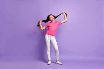 Full length body size photo of smiling schoolgirl holding long brunette hair wearing casual clothes isolated on purple color background