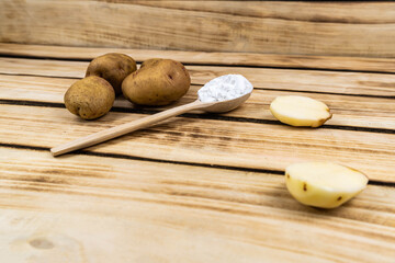 Wooden spoon with starch and a bunch of potatoes on a wooden background.