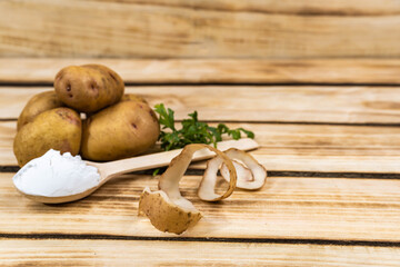 Obraz na płótnie Canvas Wooden spoon with starch and a bunch of potatoes on a wooden background.