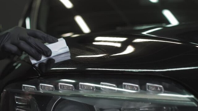 Car detailing - Man applies nano protective coating or wax on black car. Covering car bonnet with a liquid glass polish