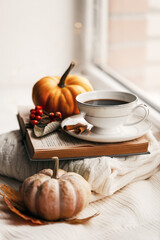 Still life of knitted woolen items, a cup of coffee and pumpkin. Dry leaves. Thanksgiving Day. Book. Morning. Fall. The concept of a cozy home holiday.