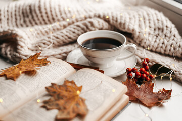Naklejka na ściany i meble Autumn morning coffee. Cup of coffee and book on a plaid against the background of autumn leaves. Still life concept.