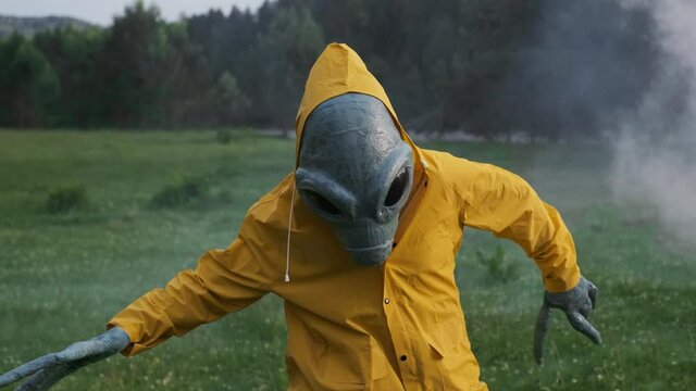 aliens dance in smoke. alien has arrived on earth and is standing in forest. an actor in alien costume, in yellow raincoat and khaki pants, touches his hands.UFO futuristic concept