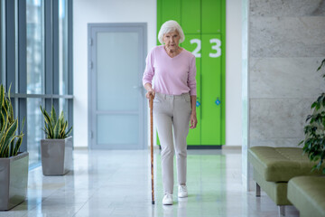 Fototapeta na wymiar Elderly woman with a walking stick walking in the corridor