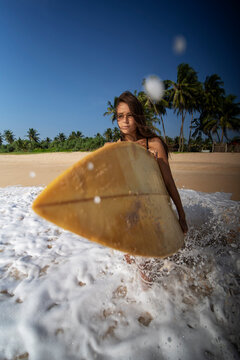 Young tanned woman enters the ocean with a surfboard. Sri Lanka