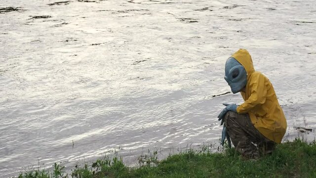alien stands by river in yellow raincoat,looks around, UFO concept, science Fiction.alien has arrived on earth.actor in alien costume