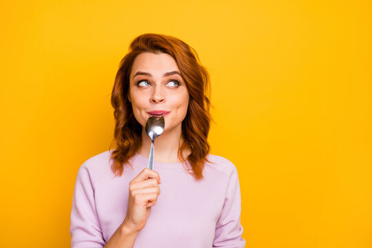Portrait of charming beautiful cute inspired positive woman hold lick spoon think thoughts about yummy breakfast look copyspace wear pink jumper isolated over yellow color background