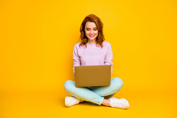 Full size photo of positive cheerful woman sit legs crossed use computer read news communicate online with colleagues family wear teal jumper isolated over yellow color background