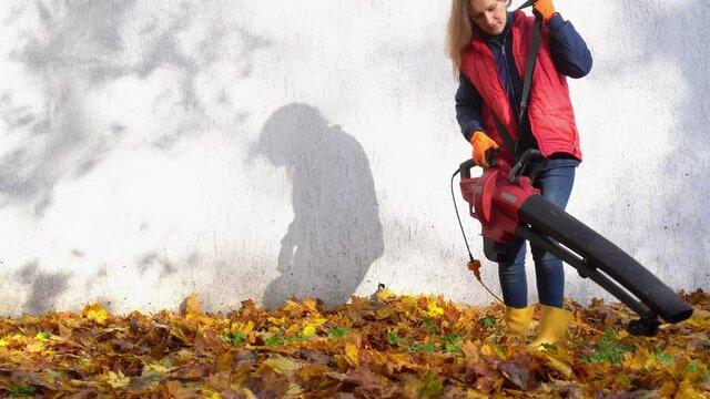 Housewife worker blowing leaves near house in autumn season.