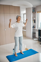 Fototapeta na wymiar Beautiful sporty female putting her hands up while standing in living room