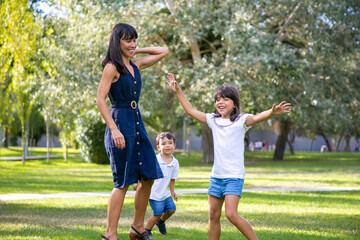 Naklejka na ściany i meble Two joyful kids and their mom playing active games on grass, having fun together in park. Family outdoor activity and leisure concept