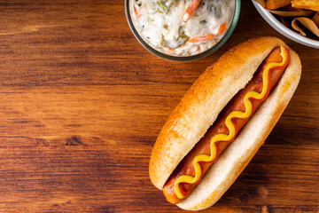 American traditional fast food Hotdog with fresh organic bread bun white wheat and black charcoal sausage ketchup mustard for meal with roasted onion pickle and French fries wedges and coleslaw