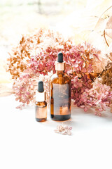 Glass bottles with oil for face and body care on pink floral background. Beauty by nature. Photo