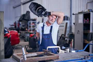 Handsome mechanic holding welding torch and protective helmet