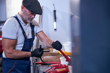 Bearded male mechanic in cap working in garage