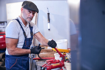 Bearded male worker assembling portable hydraulic jack in garage