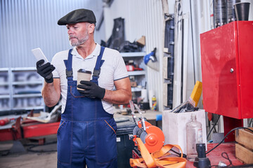 Bearded mechanic using mobile phone in auto repair shop