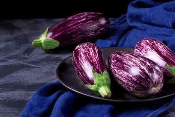 Graffiti eggplants on the black plate on the grey table. Dark photo