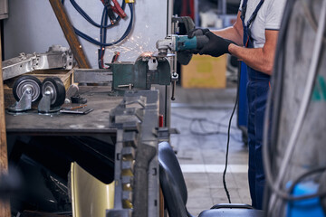 Fototapeta na wymiar Mechanic grinding car metal parts in garage
