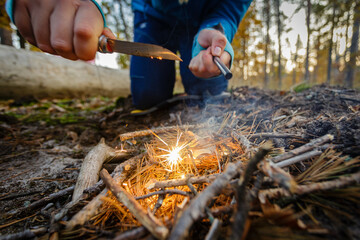 Obraz premium Man outdoors makeing fire by flint. View from above. Flying sparks.