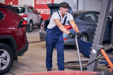 Bearded auto mechanic using hydraulic car lift in garage