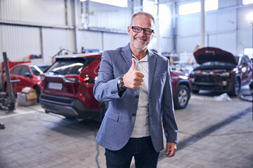 Cheerful man showing approval gesture at car repair service station