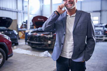 Joyful man talking on mobile phone in auto repair shop