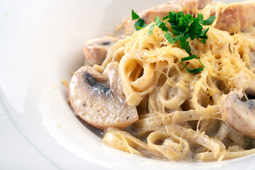 Pasta spaghetti with mushrooms and herbs in cream sauce in a white plate, close up