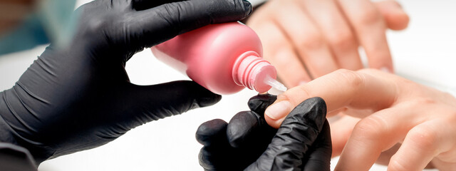 Nail treatment by cuticle oil while manicure of young woman in nail salon