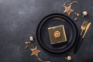 Christmas table setting with black ceramic plate, gift box and gold accessories on black stone...