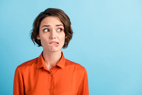 Closeup photo of sad depressed displeased lady horrified facial expression made huge big mistake feel guilty look side empty space bite lips wear orange shirt isolated blue color background