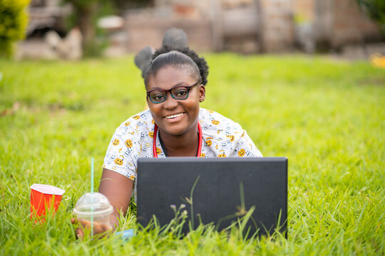 image of beautiful, cheerful  african lady, in front of laptop in a greenfield