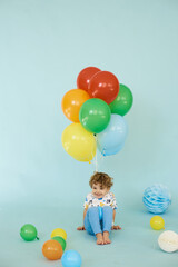Fototapeta na wymiar Full length portrait of cheerful boy holding balons posing against blue background