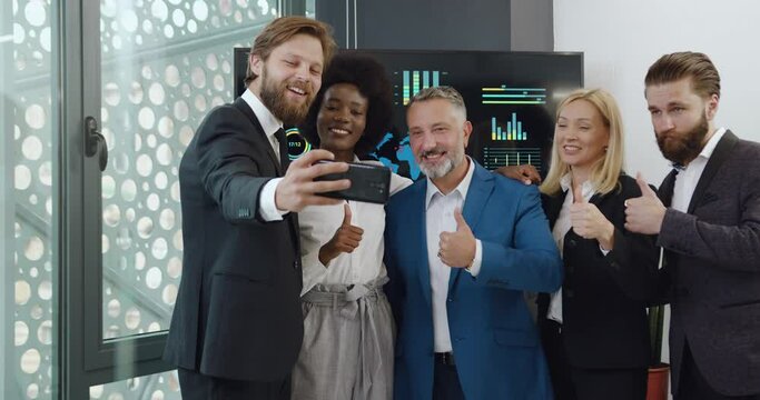 Good-tempered smiling successful professional multiracial businesspeople taking a selfie in modern meeting room