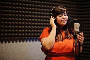 Young asian singer with microphone recording song in record music studio.