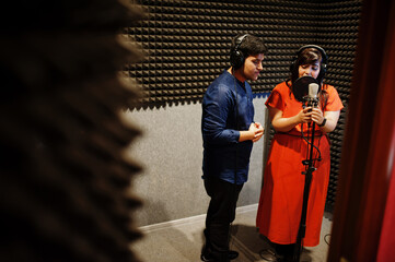 Young asian duet singers with microphone recording song in record music studio.